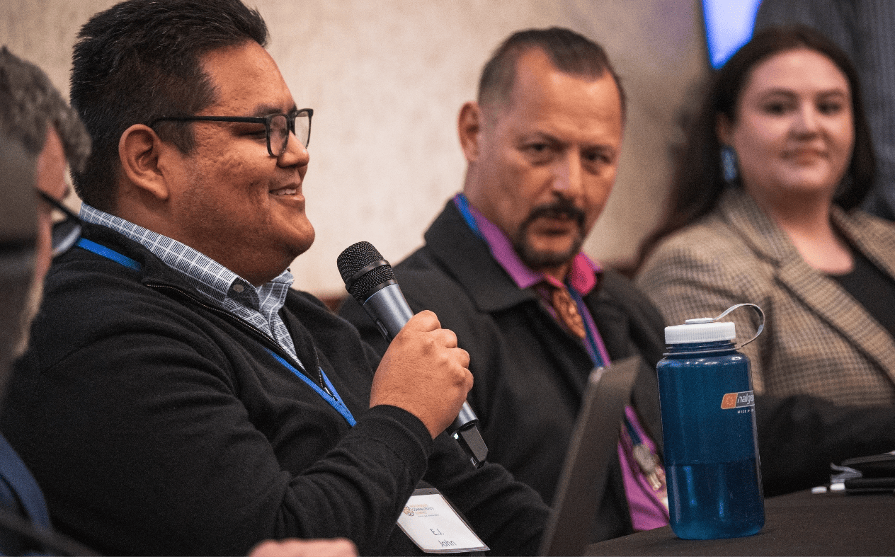 Navajo man smiles as he speaks into a microphone while addressing attendees of the Indigenous Connectivity Summit 2023, in Anchorage, Alaska.